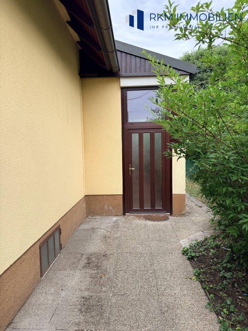 Seitlicher Eingangsbereich des Hauses mit brauner Tür und kleinem Fenster.