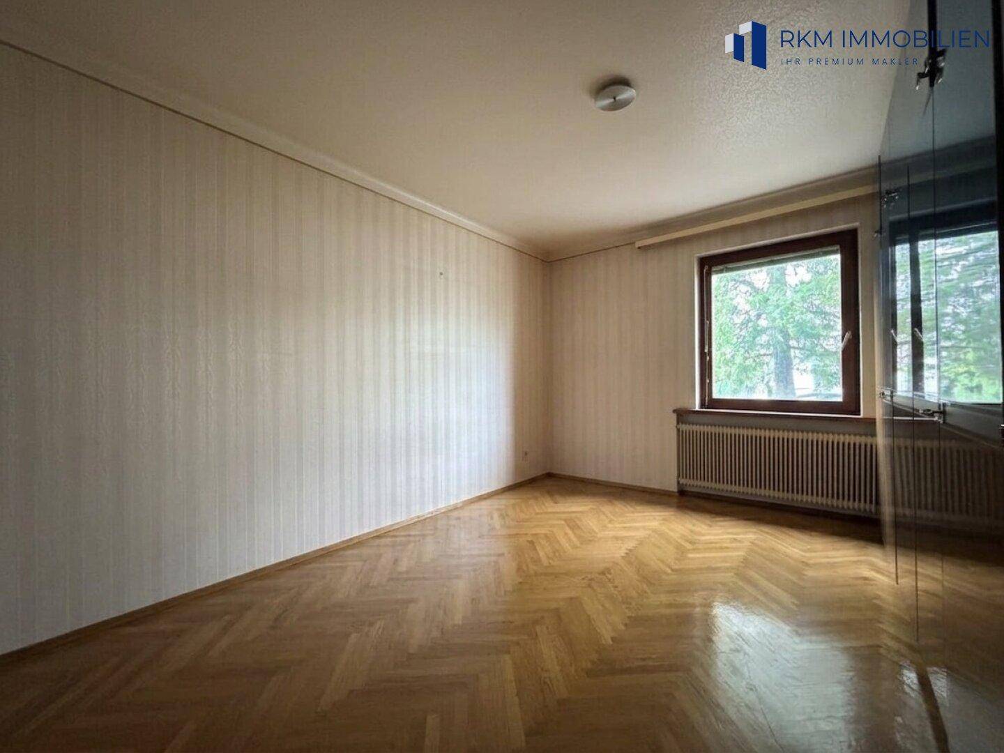 Geräumiges Zimmer mit glänzendem Fischgrätparkett und einem großen Fenster.