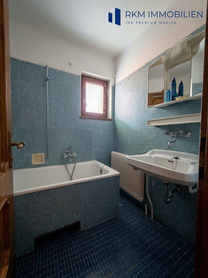 Badezimmer mit blauen Mosaikfliesen, Badewanne und Waschbecken.