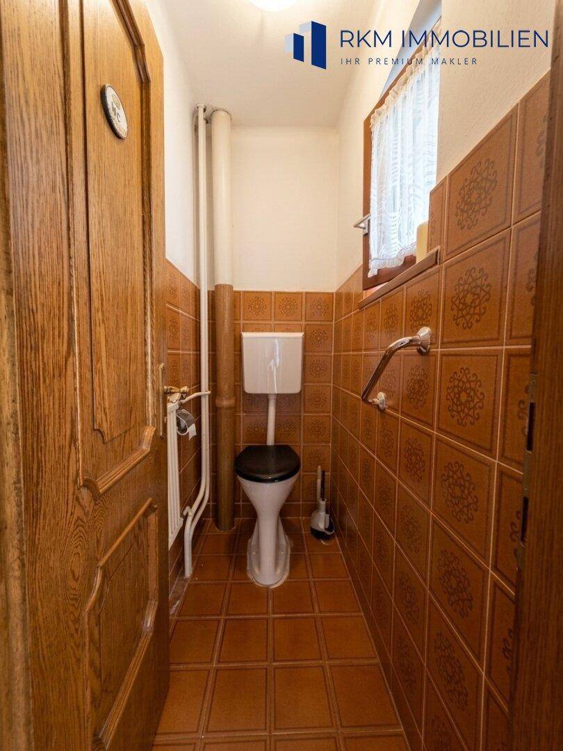 Separate Toilette mit braunen Fliesen, Fenster und Haltegriffen.