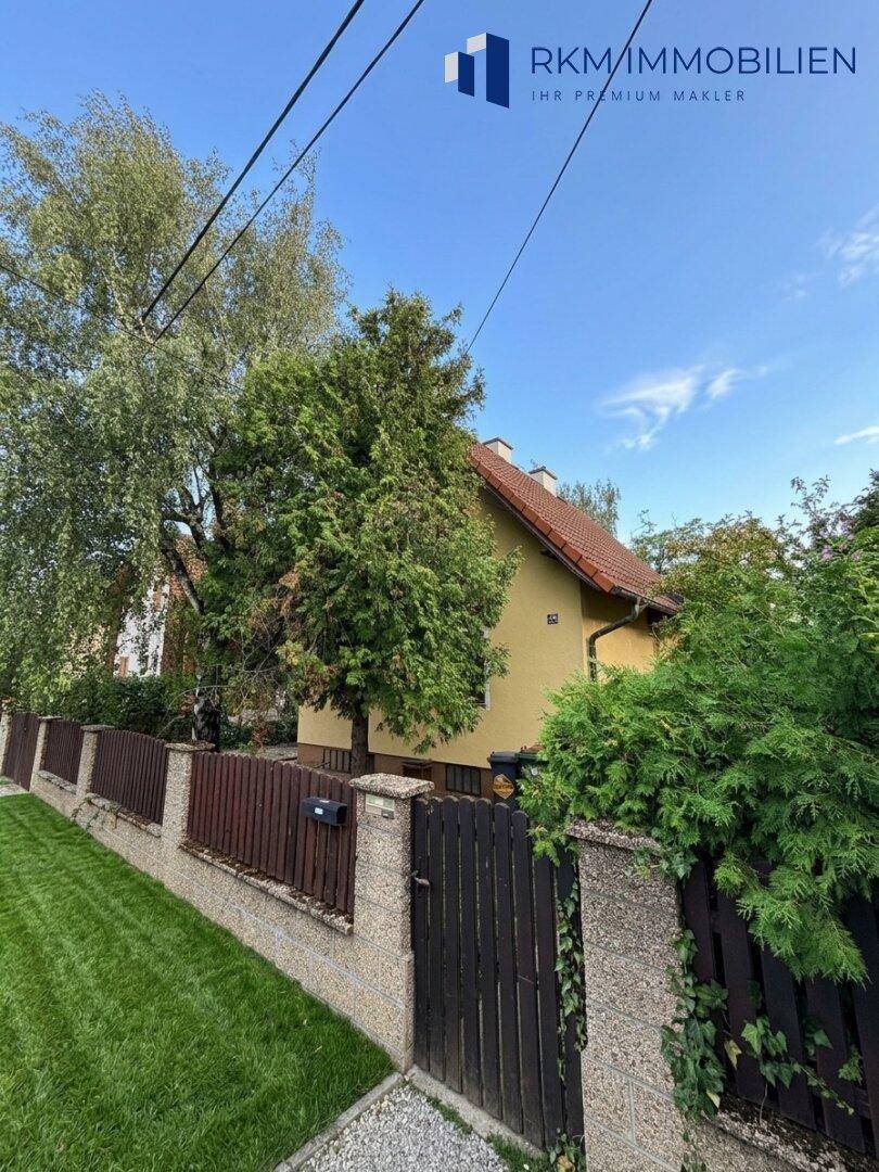Ansicht des Hauses von der Straße mit Zaun und üppiger Bepflanzung.