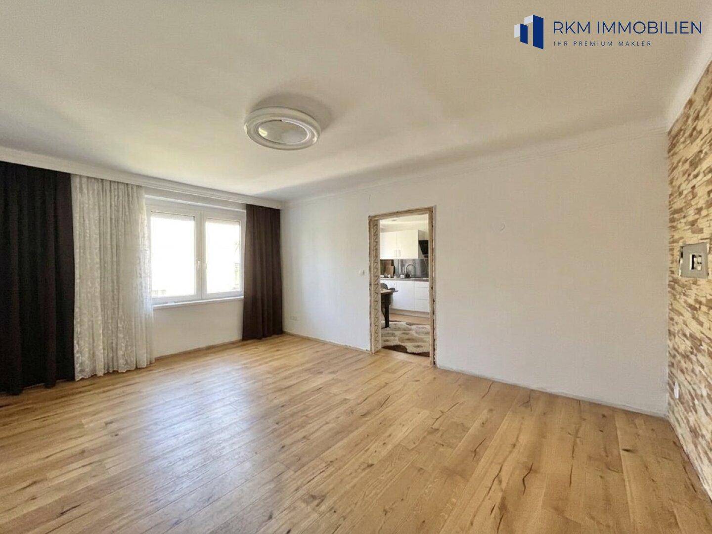 Helles Wohnzimmer mit Holzboden und strukturierten Tapetenakzenten an der Wand.