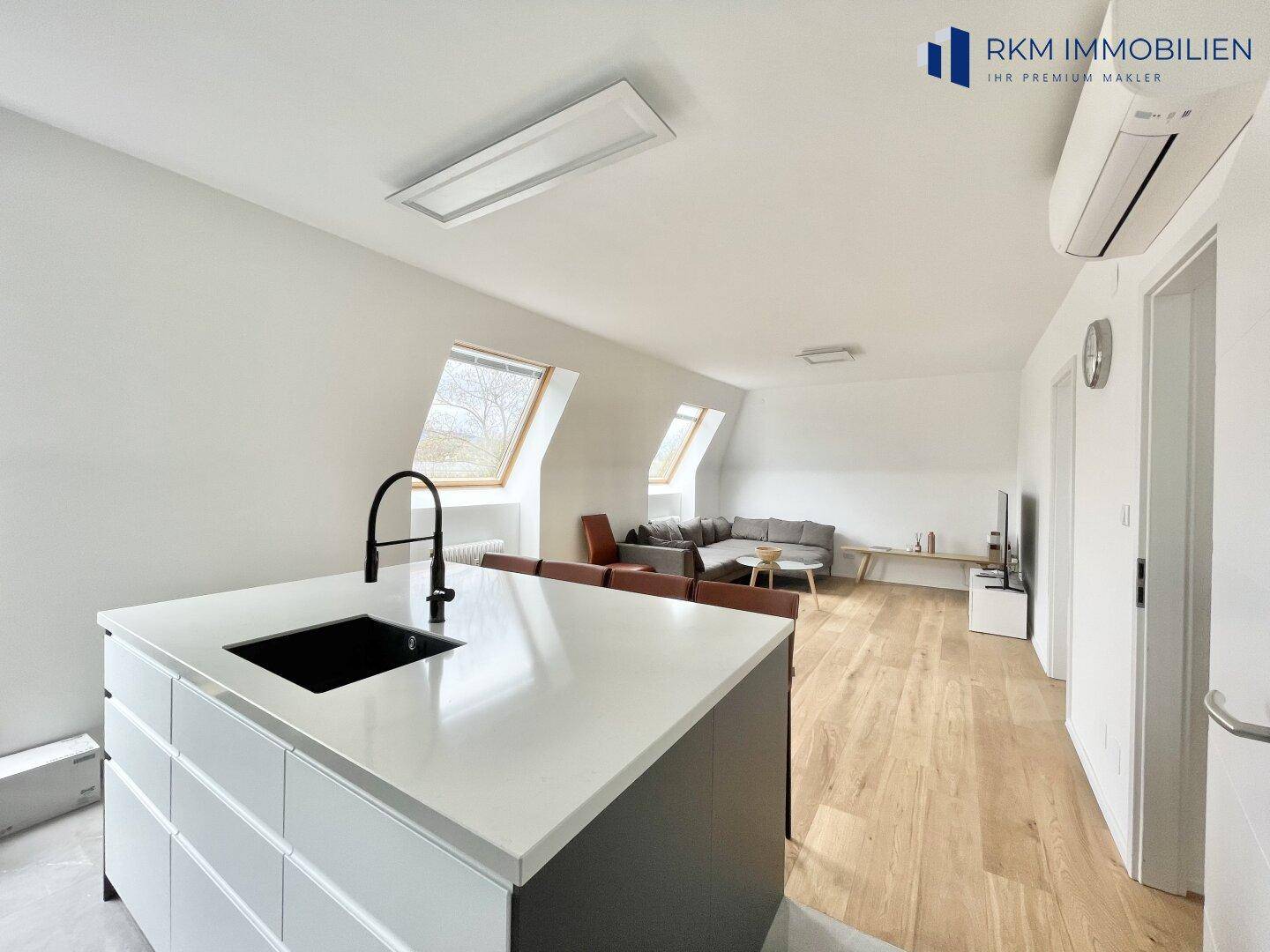 Offener Wohnbereich mit moderner Küche, Holzboden und Dachfenstern, ideal für geselliges Beisammensein.
