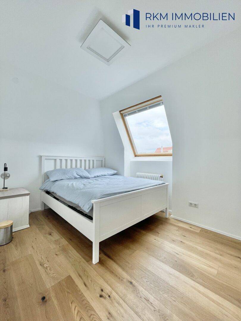 Helles Schlafzimmer mit weißem Bett, Holzboden und einem Dachfenster für viel Tageslicht.