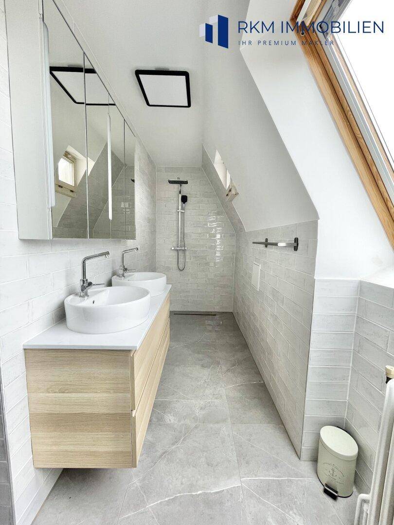Helles Badezimmer mit Doppelwaschbecken, ebenerdiger Dusche und modernen grauen Fliesen.