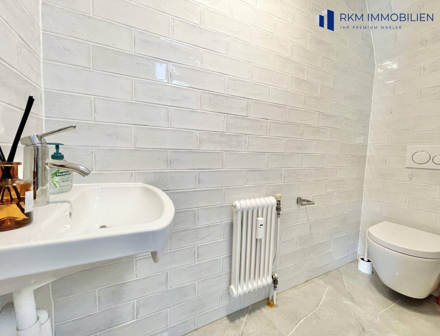 Modernes Gäste-WC mit Waschbecken, Toilette und stilvollen grauen Wandfliesen.