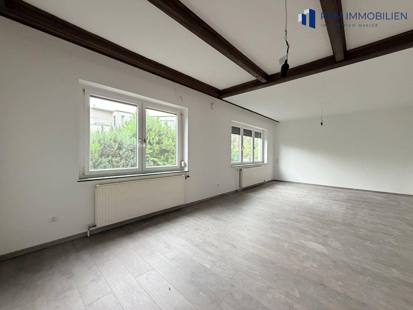 Geräumiges Zimmer mit sichtbaren Holzbalken an der Decke und Laminatboden.