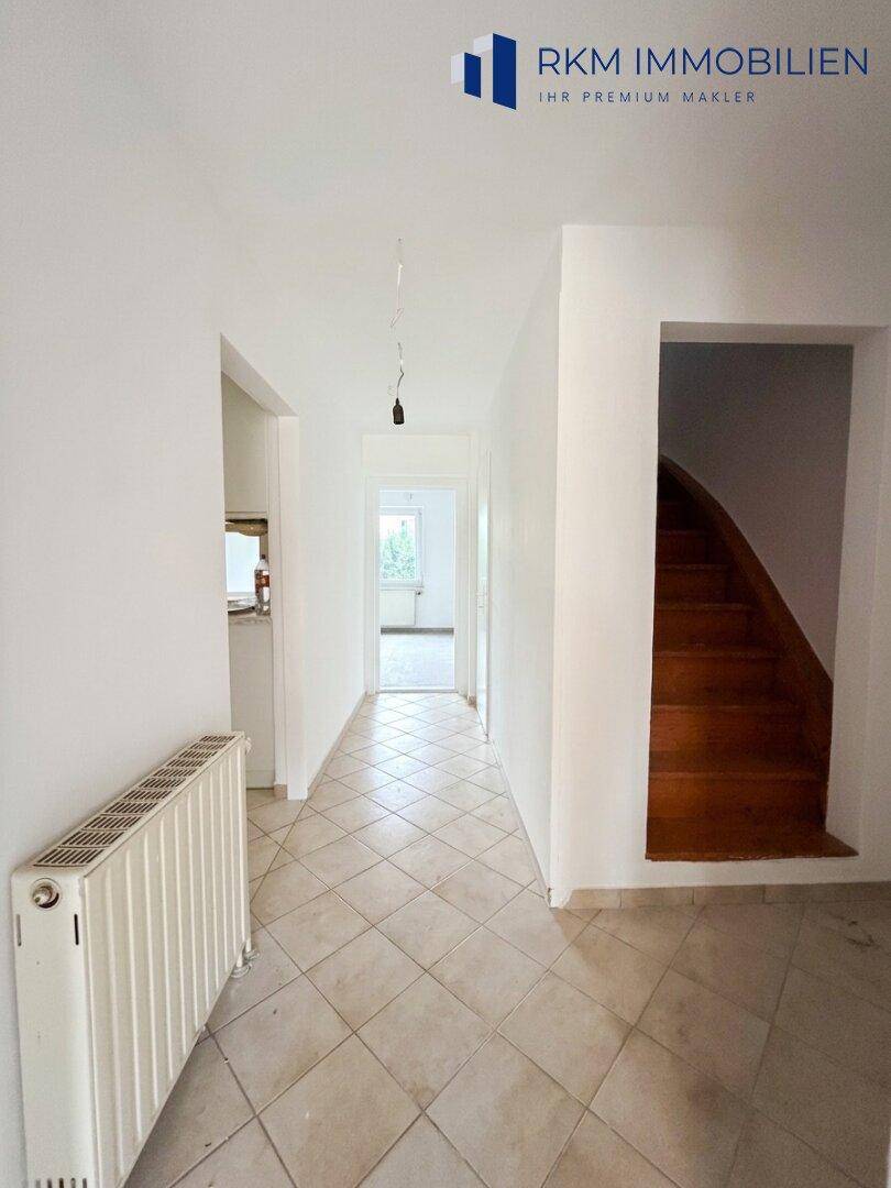 Heller Flur mit Fliesenboden und einer Holztreppe, die in die oberen Stockwerke führt.