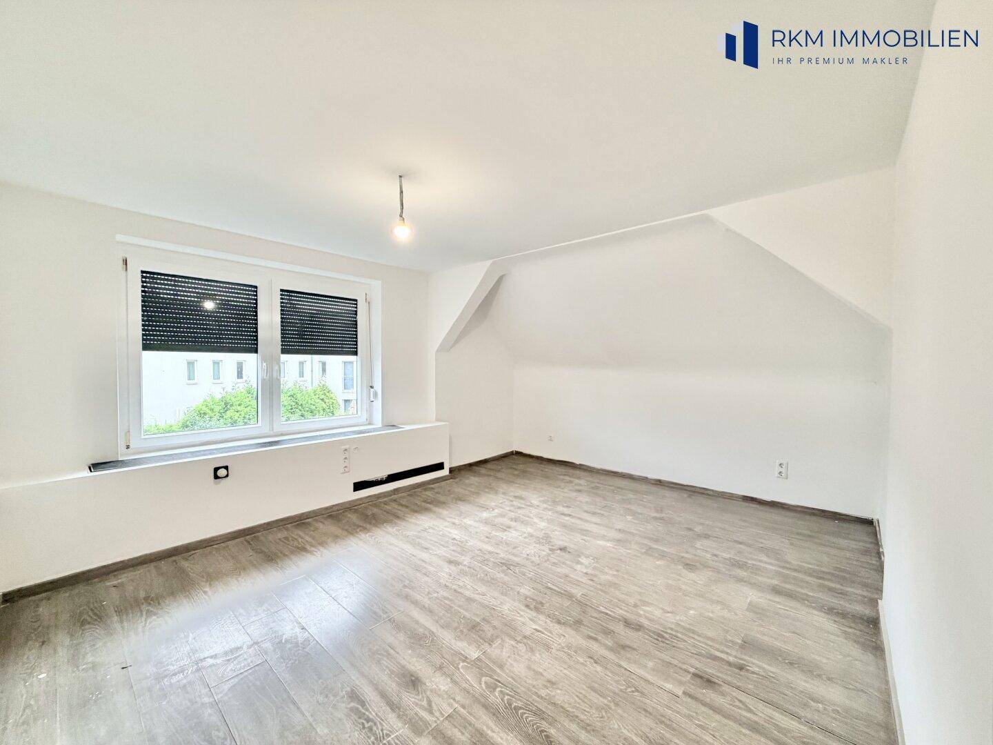 Helles Schlafzimmer im Dachgeschoss mit schrägen Wänden, Laminatboden und großem Fenster.