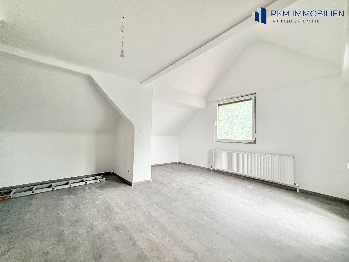 Geräumiges Dachzimmer mit schrägen Wänden, Laminatboden und einem Fenster.
