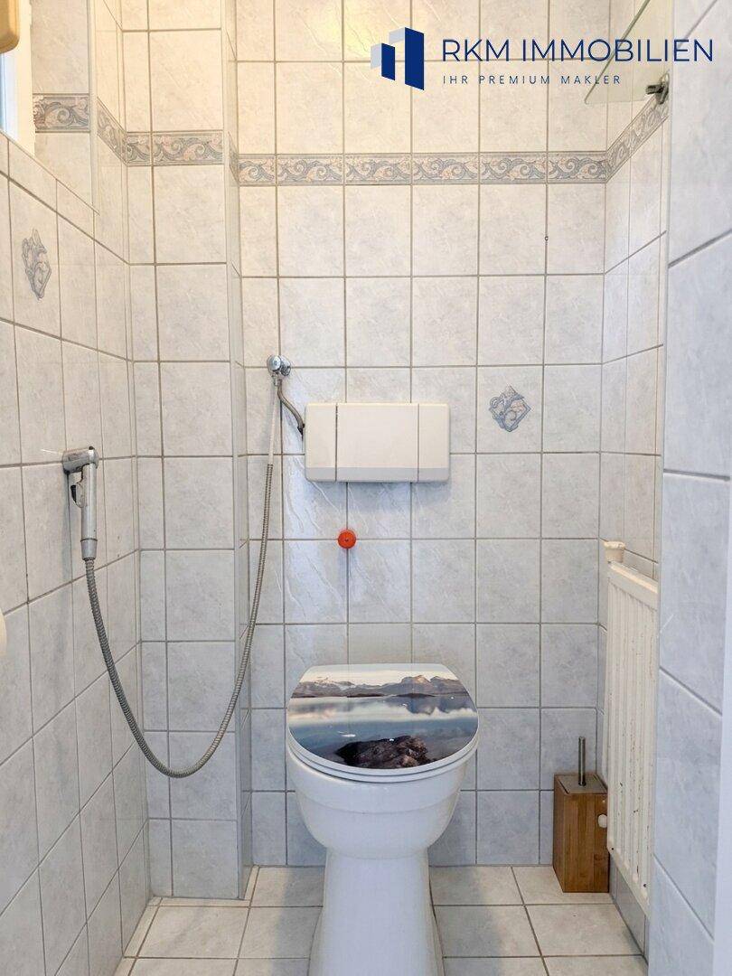 Separates WC mit weißen Fliesen, Toilette und Bidet-Duschfunktion.
