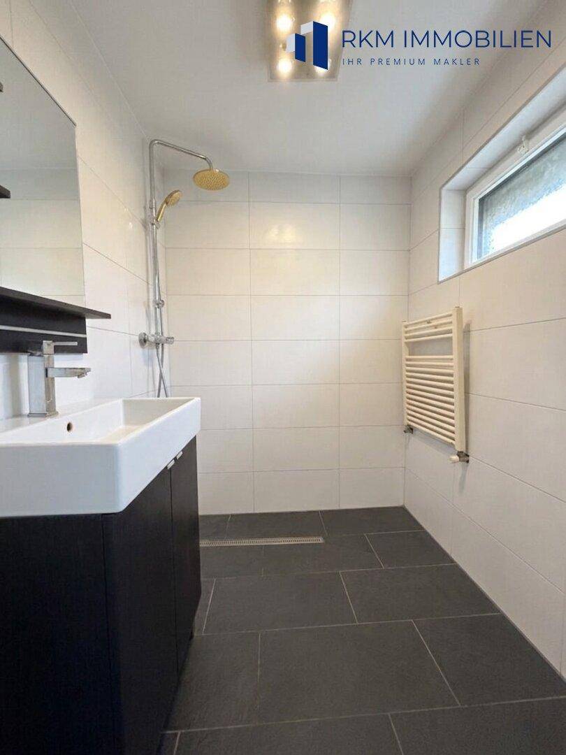 Modernes Badezimmer mit ebenerdiger Dusche, dunklen Fliesen und beheiztem Handtuchhalter.