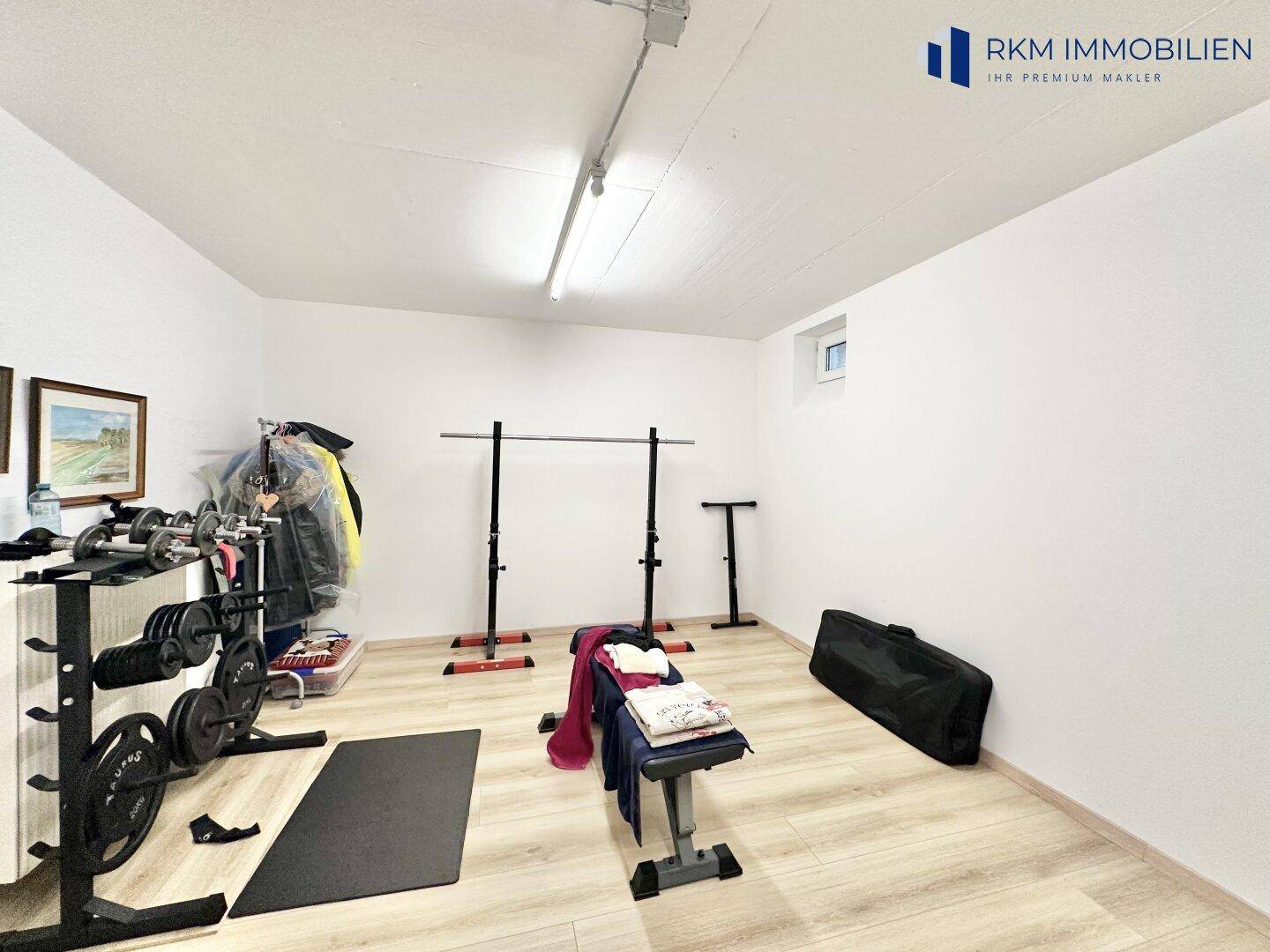 Geräumiger Fitnessraum im Untergeschoss mit Sportgeräten und hellem Boden.
