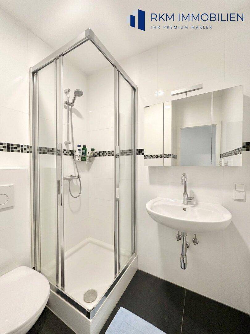 Helles Badezimmer mit Duschkabine, WC, Waschbecken und weißen Fliesen.