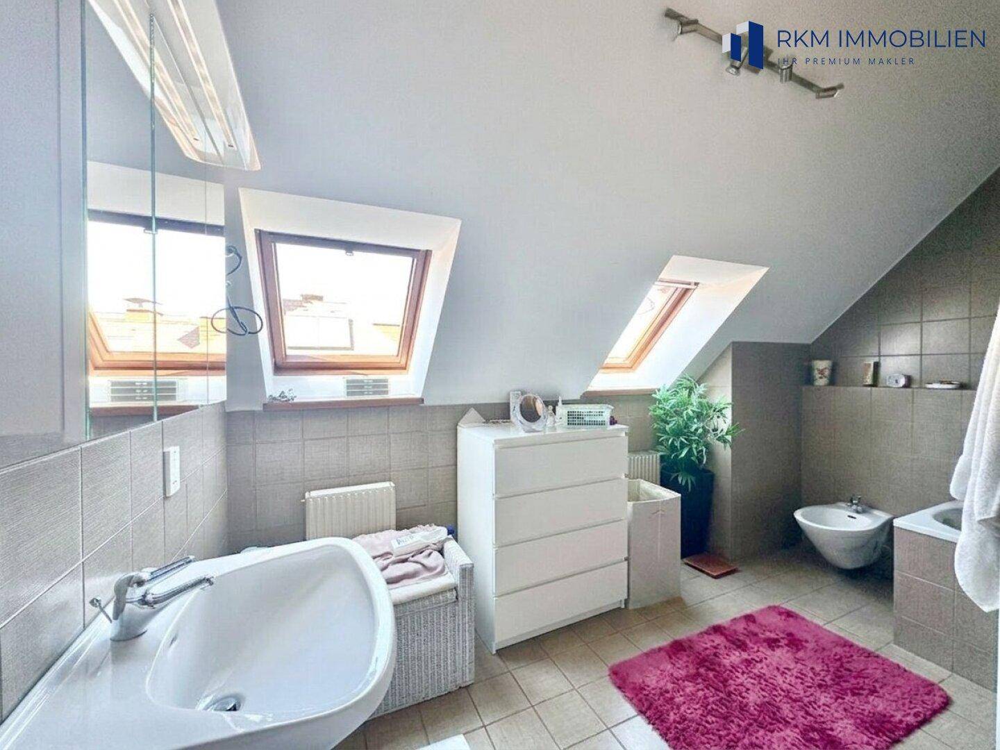 Badezimmer im Dachgeschoss mit Fliesenboden, Waschbecken, Bidet und Dachfenstern.