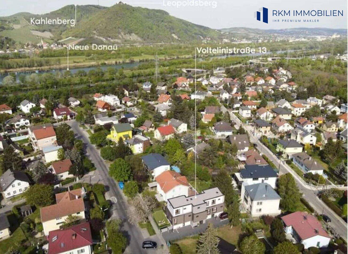 Luftaufnahme des Wohngebiets Voltelinistraße 13 mit Blick auf die Neue Donau und die umliegenden Hügel.