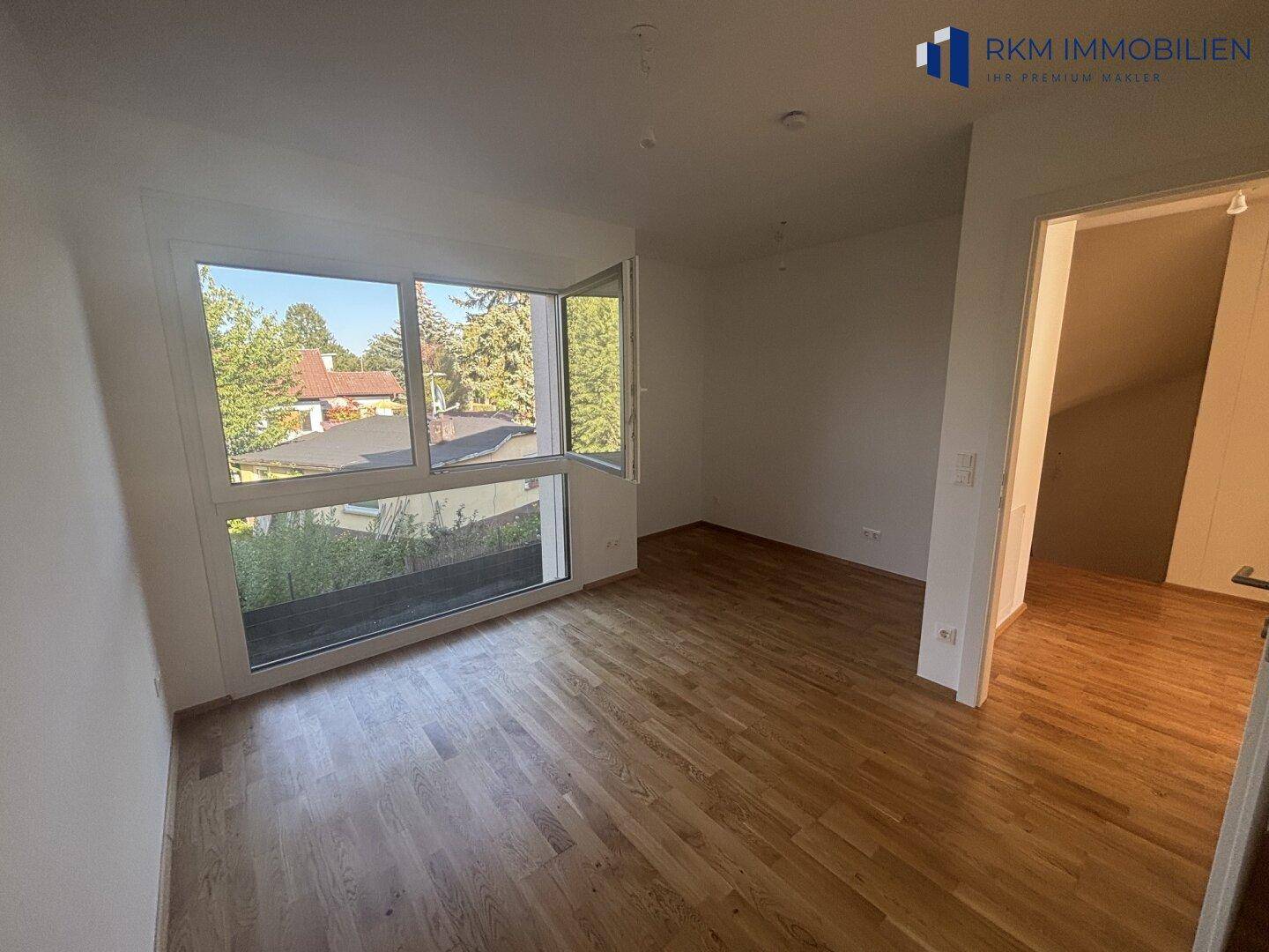 Helles Schlafzimmer mit Eichenparkett und Ausblick ins Grüne durch die geöffneten Fenster.