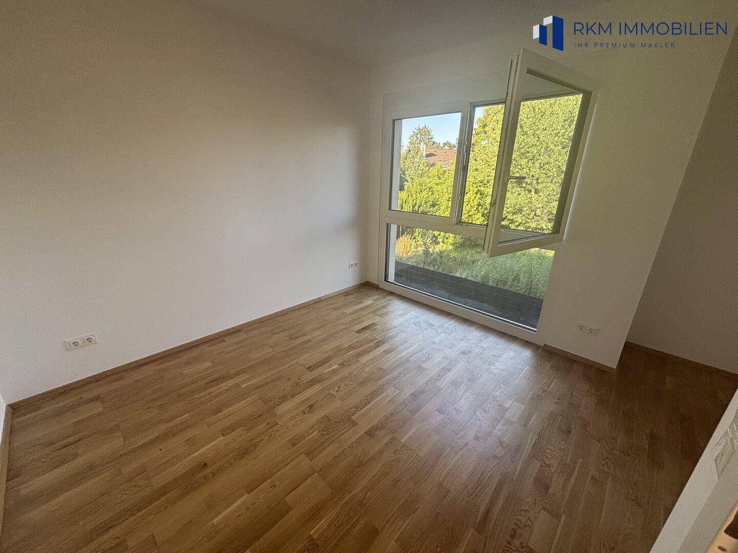Schlafzimmer mit hellem Eichenparkett und großen Fenstern, die viel Licht hereinlassen.