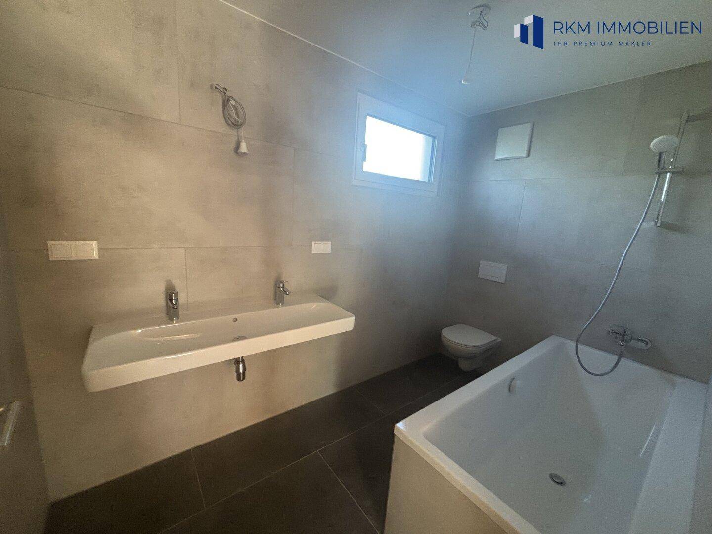 Helles Badezimmer mit Doppelwaschbecken, Badewanne und Fenster für natürliche Belüftung.