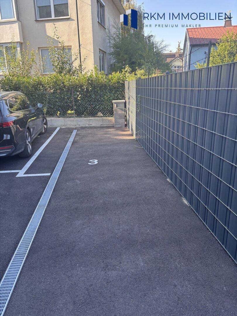 Privater Außenstellplatz mit Markierung und Zaun neben dem Gebäude.