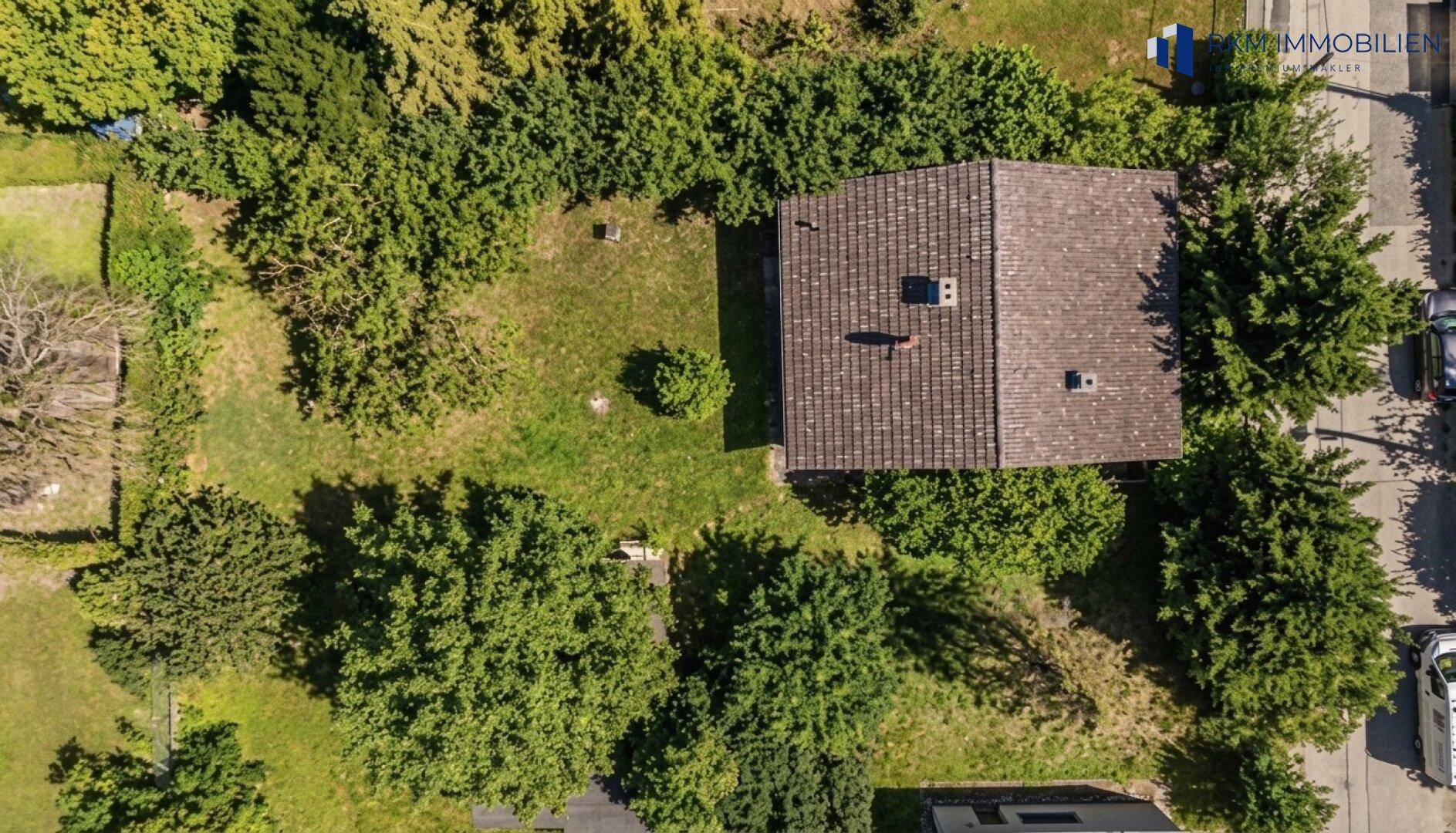 Luftaufnahme eines Einfamilienhauses mit Photovoltaikanlage auf dem Dach, umgeben von viel Grün.