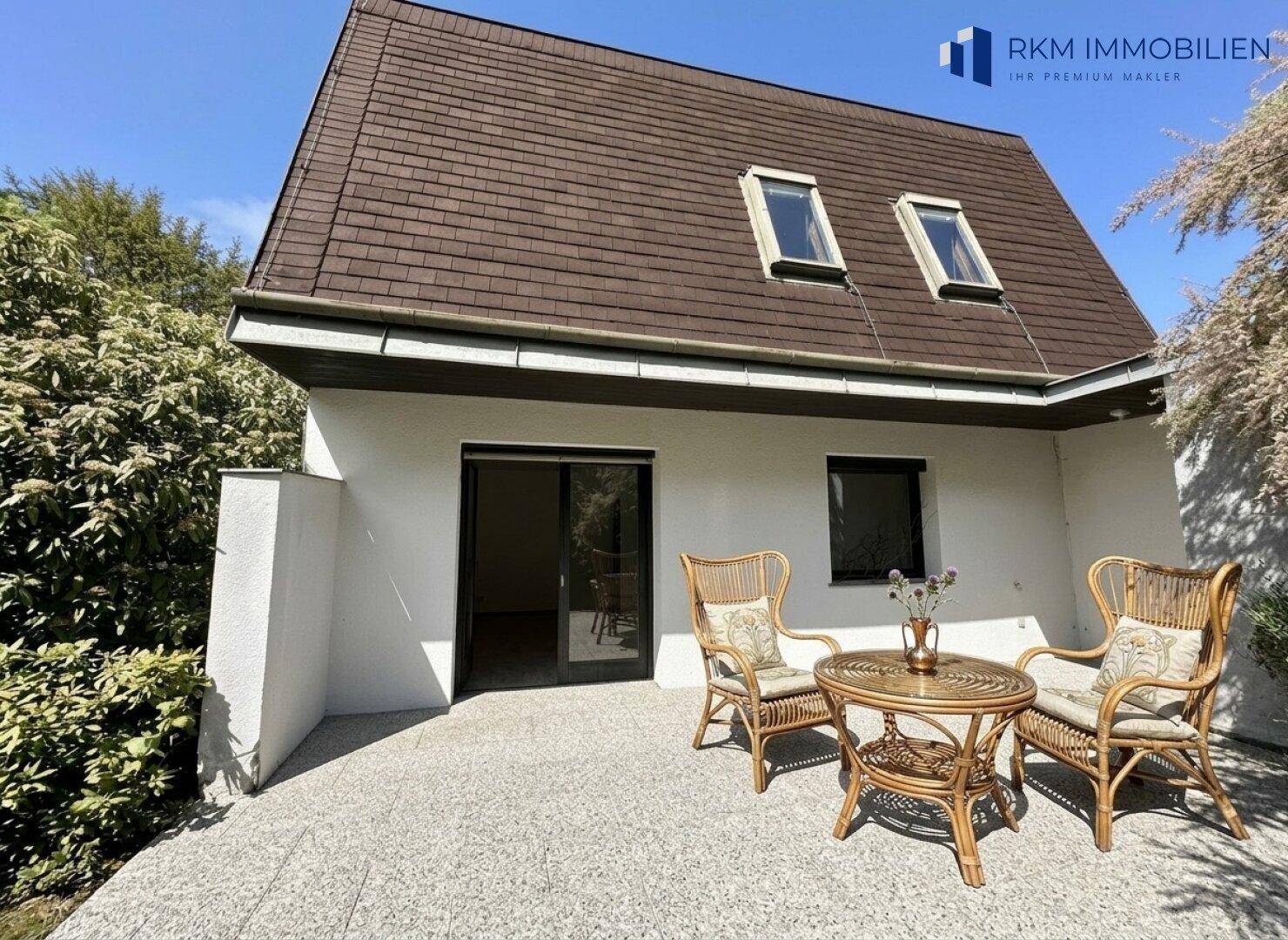 Gemütliche Terrasse mit Korbmöbeln und Zugang zum Haus, umgeben von viel Grün.