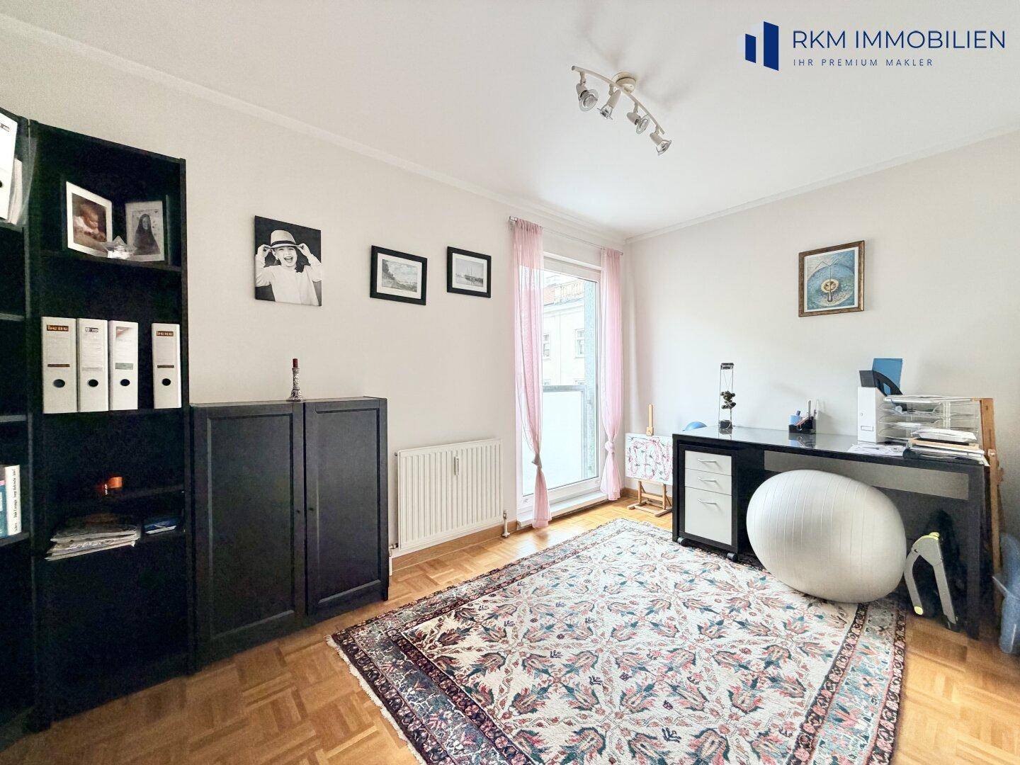 Helles Arbeitszimmer mit Parkettboden, Bücherregal und Zugang zum Balkon.