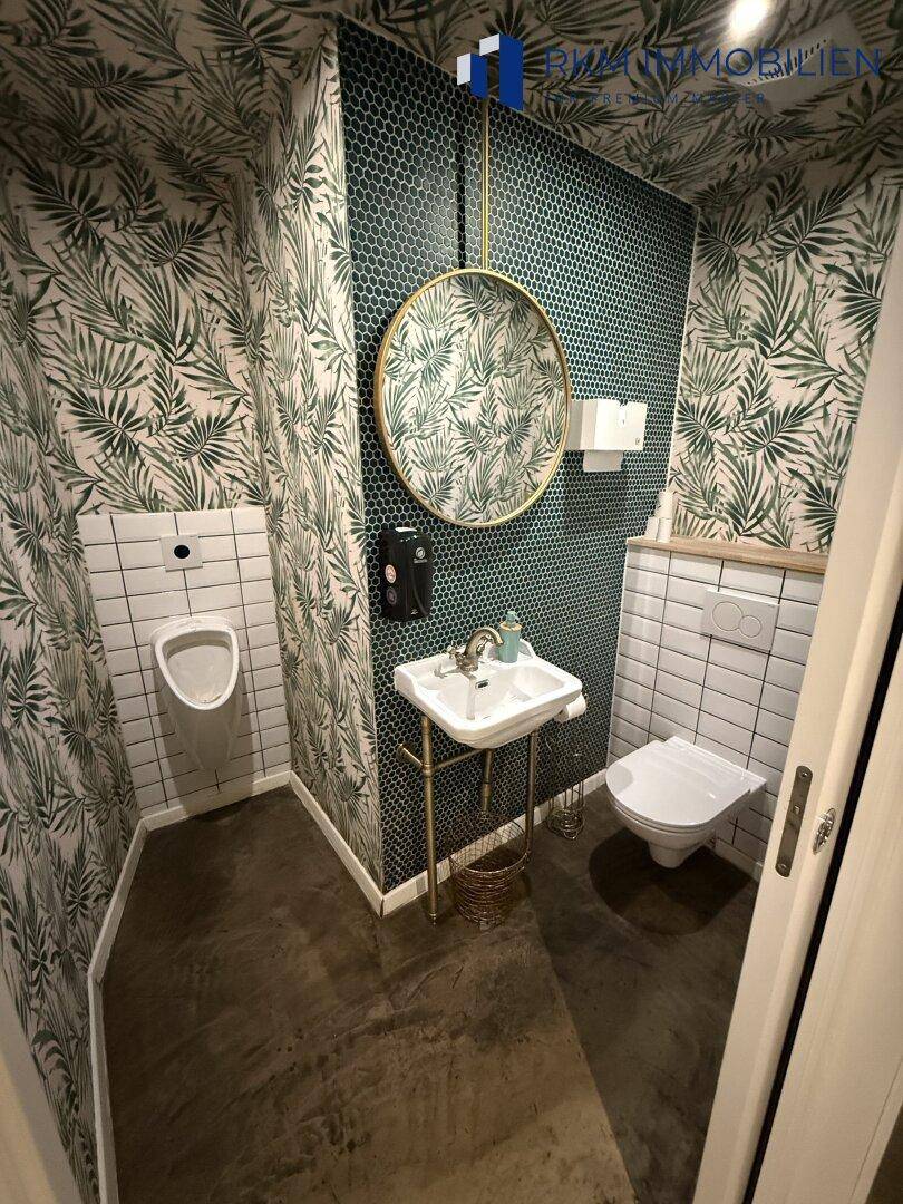 Modern gestaltete Gästetoilette mit Urinal, WC, Waschbecken und auffälliger tropischer Tapete.