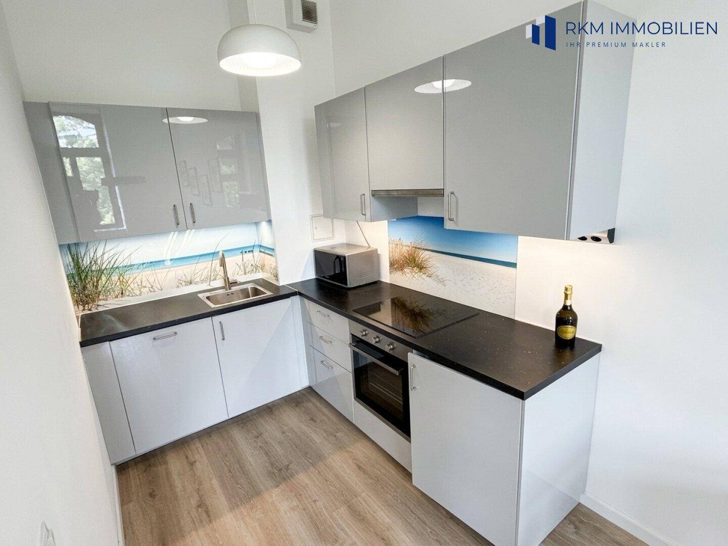 Moderne Einbauküche mit glänzenden grauen Fronten, Induktionskochfeld und Strandmotiv-Rückwand.