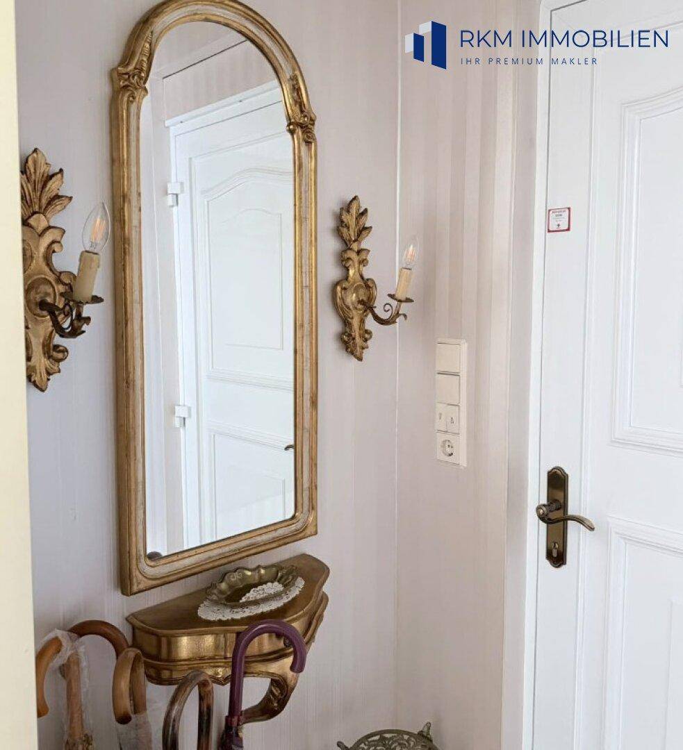 Eingangsbereich mit einem eleganten goldenen Spiegel, passender Konsole und dekorativen Wandleuchten.