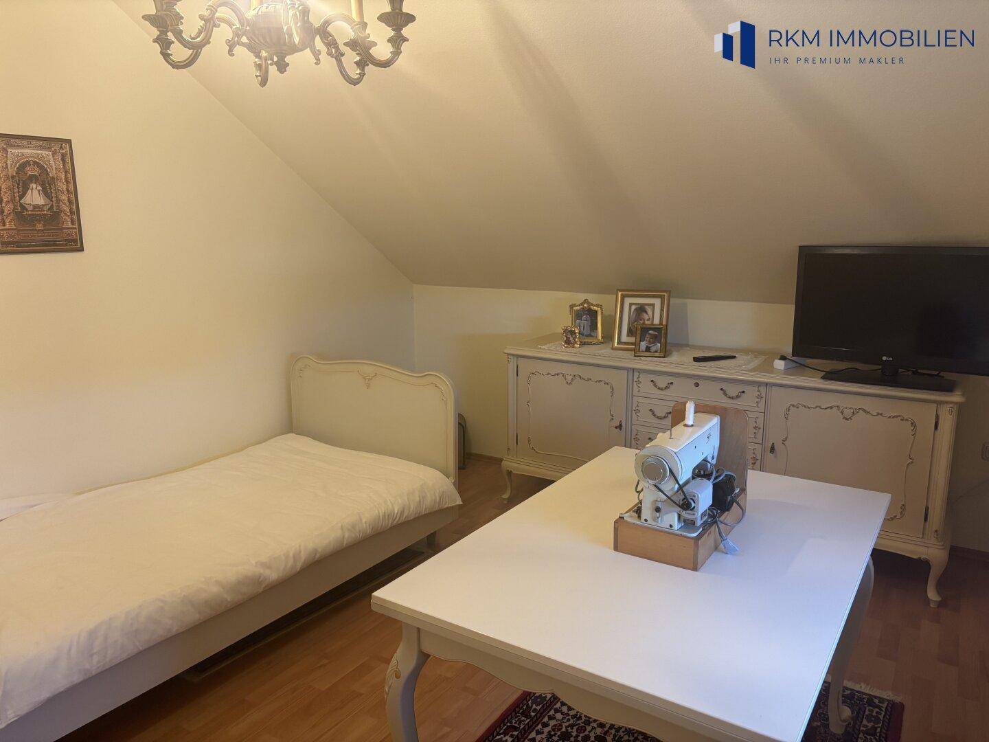 Dachzimmer mit Einzelbett, Kommode und einem Tisch, ideal als Gäste- oder Arbeitszimmer nutzbar.