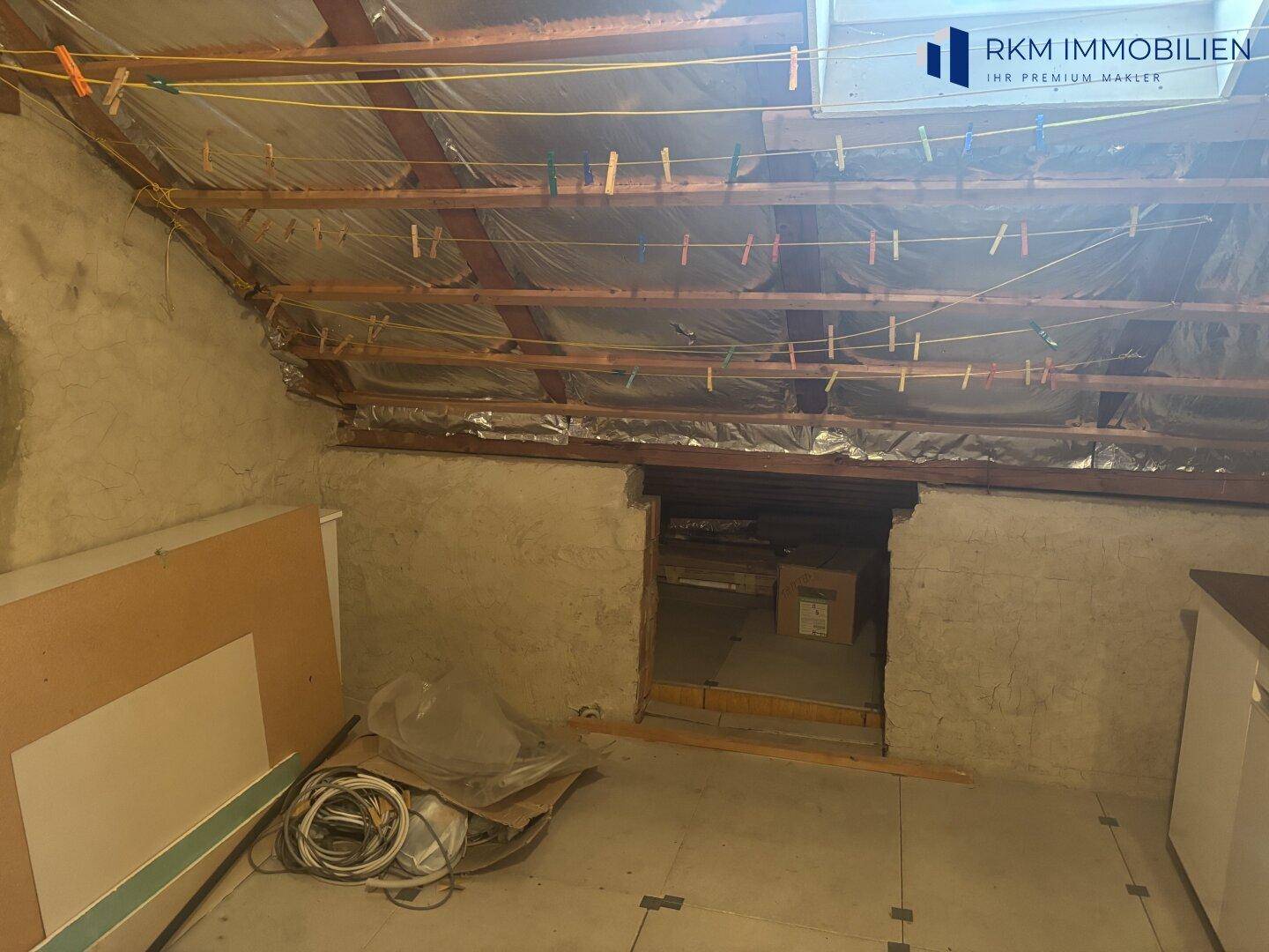Unausgebauter Dachboden mit sichtbarer Holzkonstruktion und Wäscheleinen, bietet Ausbaupotenzial.