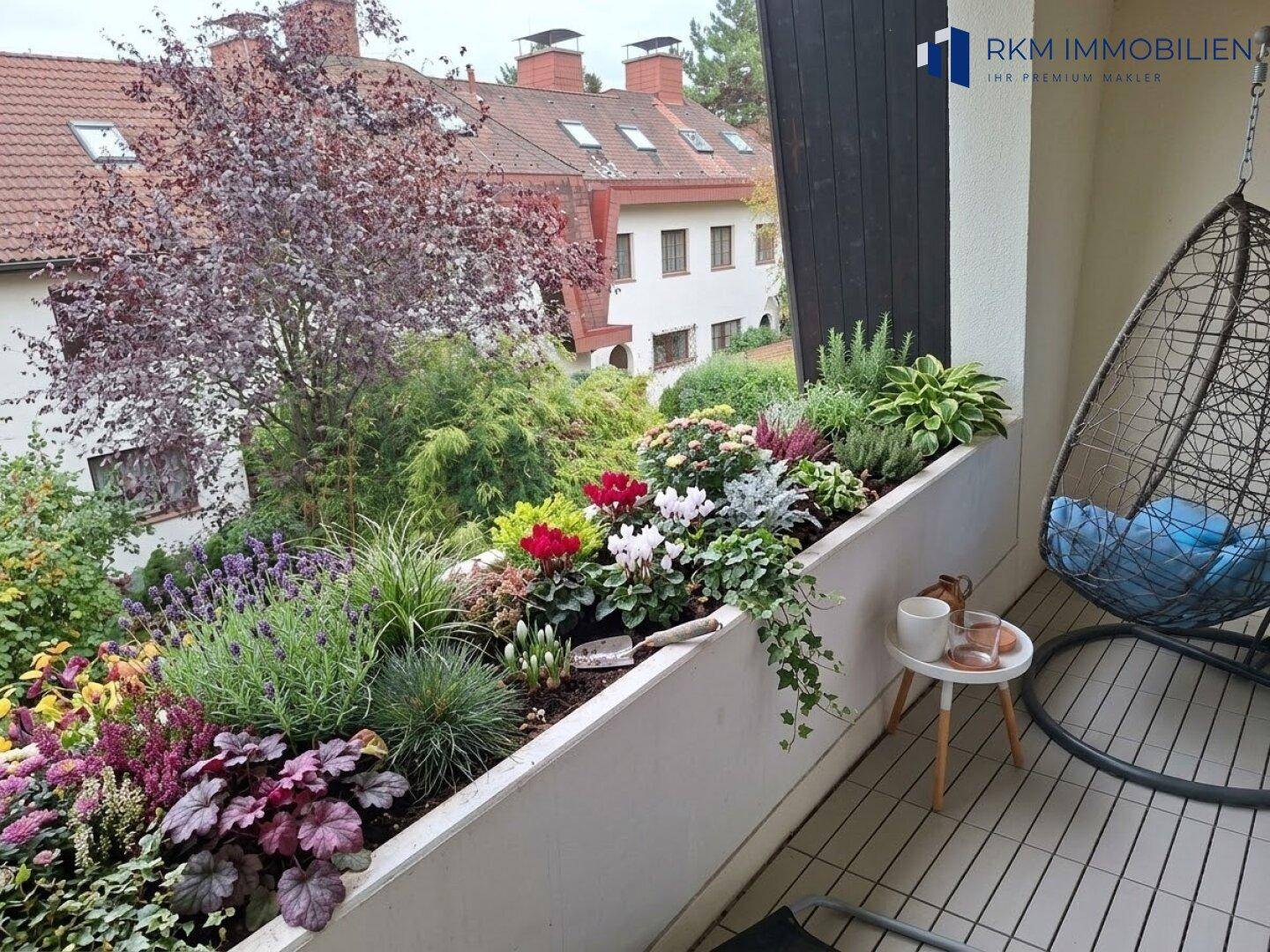 Farbenfroher Balkon mit üppigen Blumenkästen und einem bequemen Hängesessel, bietet eine grüne Aussicht.