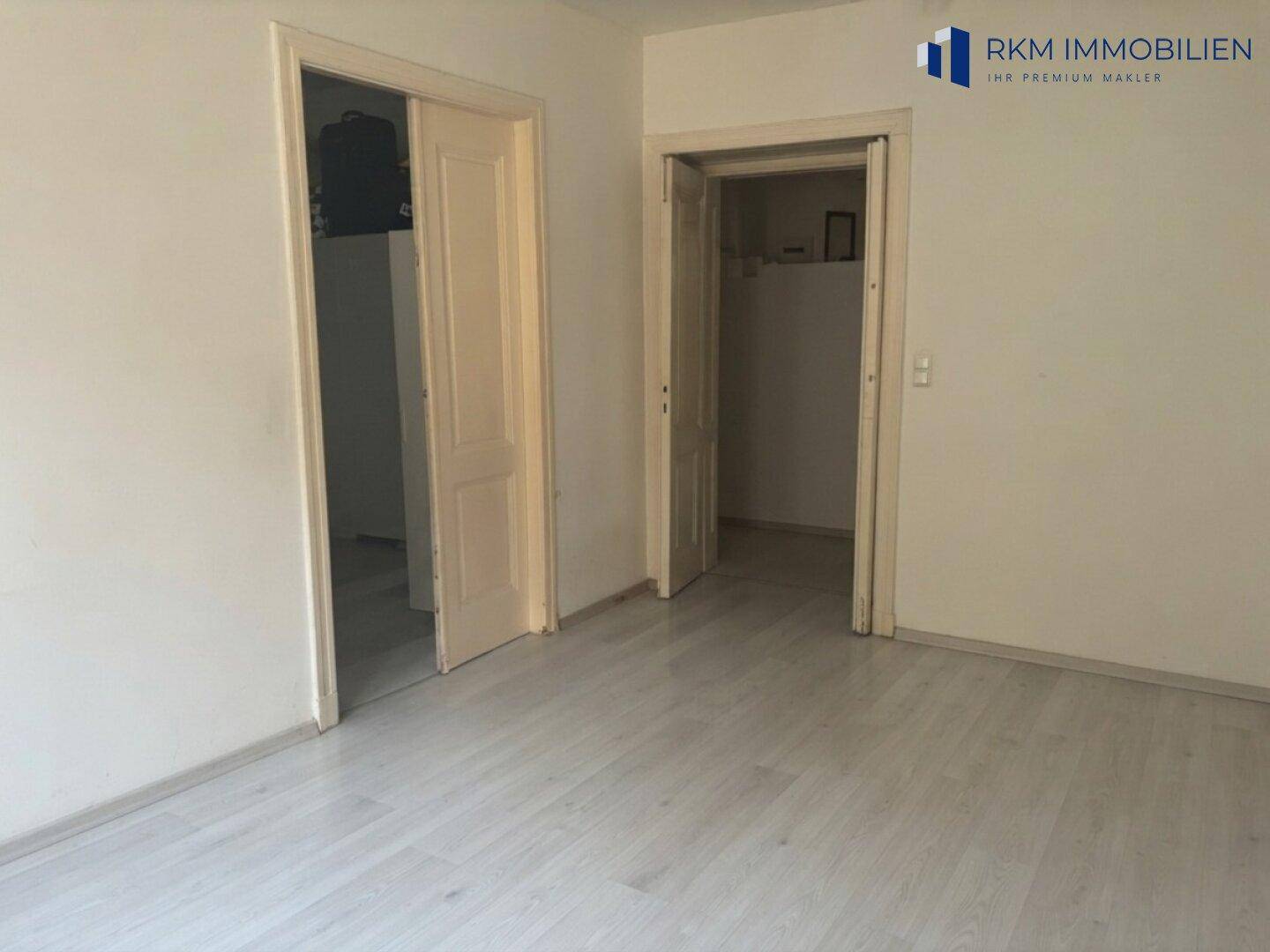 Leeres Zimmer mit zwei Türen und hellem Laminatboden, bereit zur individuellen Gestaltung der Wohnfläche.
