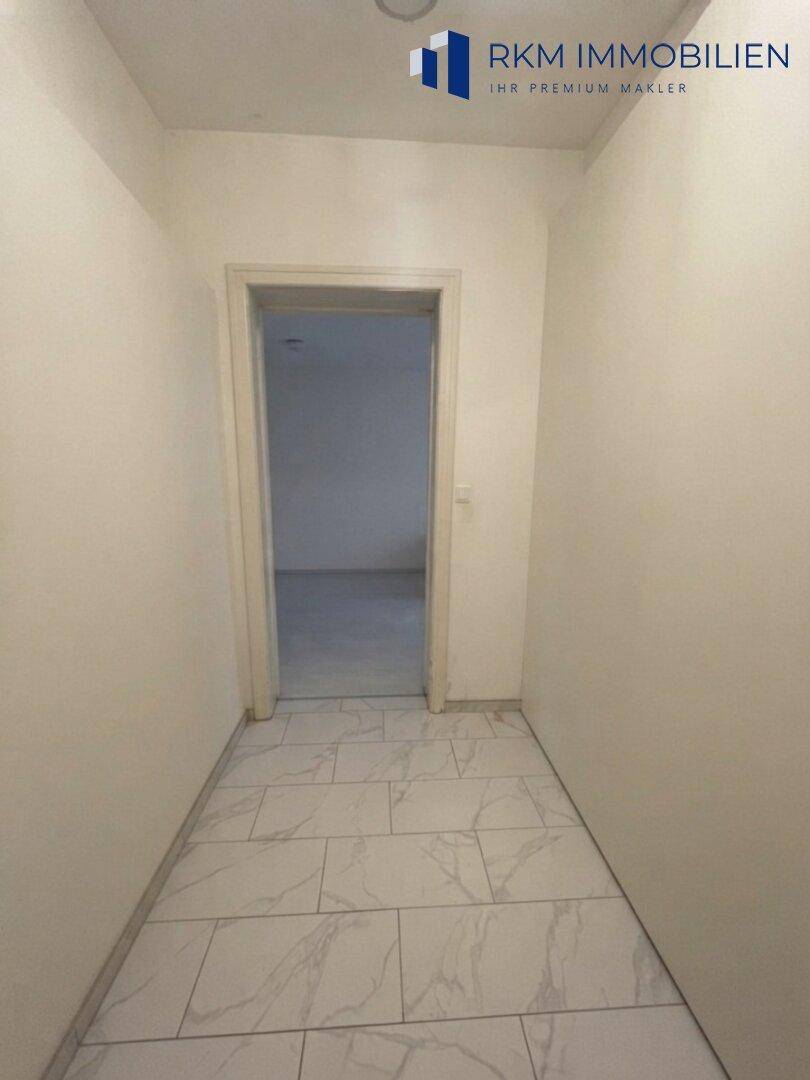 Schmaler Flur mit hellen Fliesen und einer Tür, die zu einem weiteren Raum der Wohnung führt.