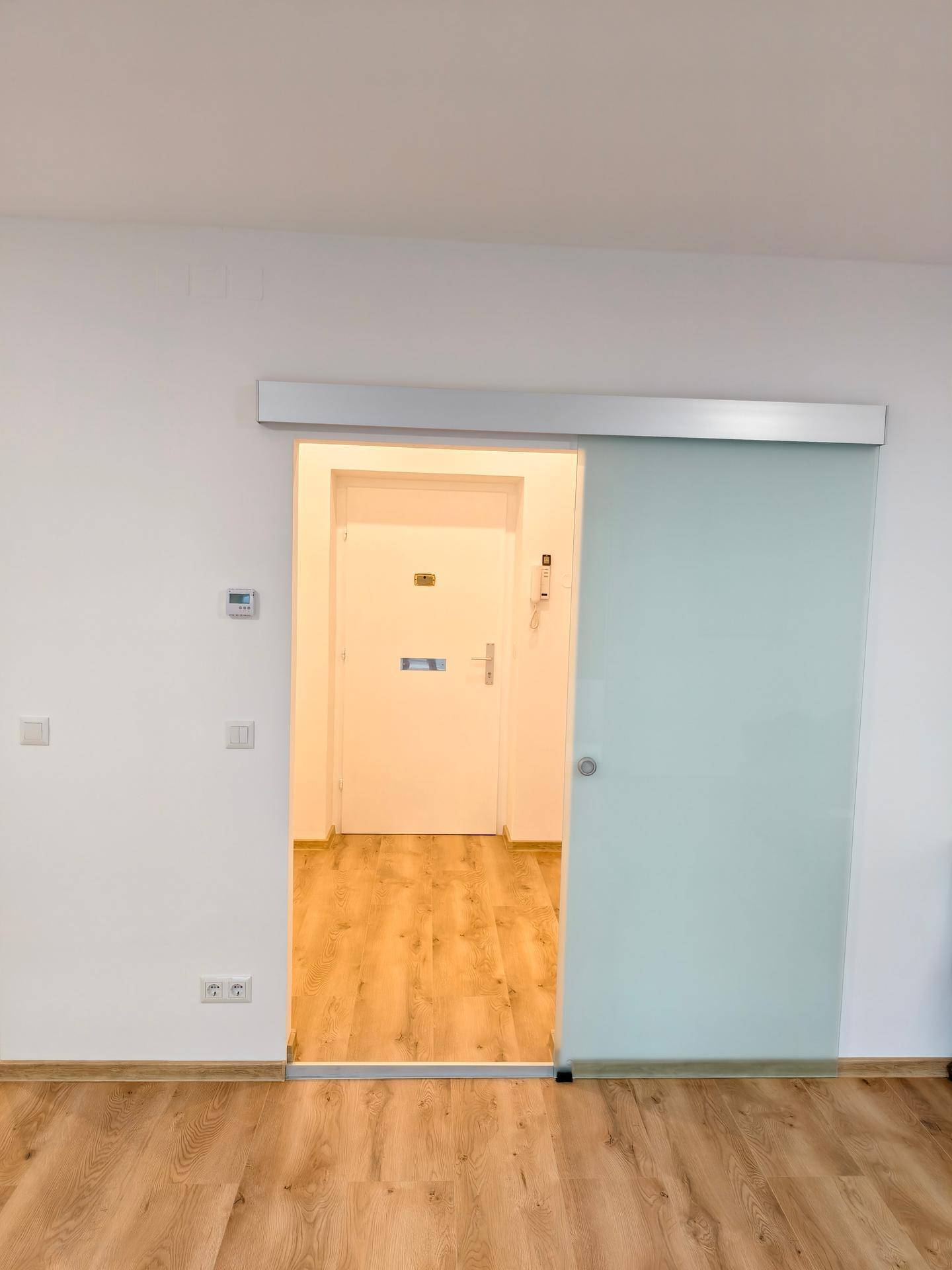 Heller Flur mit moderner Glasschiebetür und Laminatboden, der zum Wohnbereich führt.