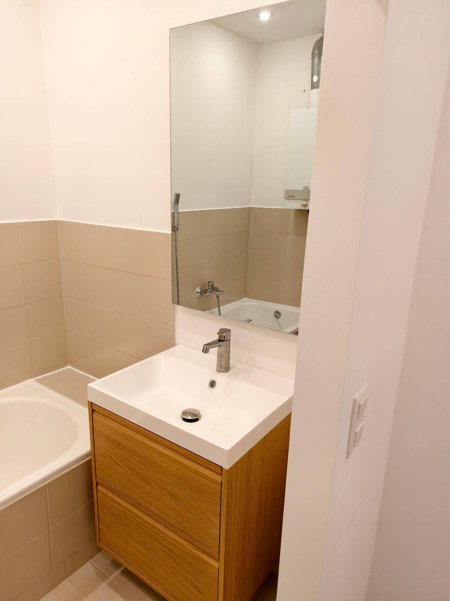 Modernes Badezimmer mit Waschtisch, großem Spiegel und Badewanne, ausgestattet mit beigen Fliesen.
