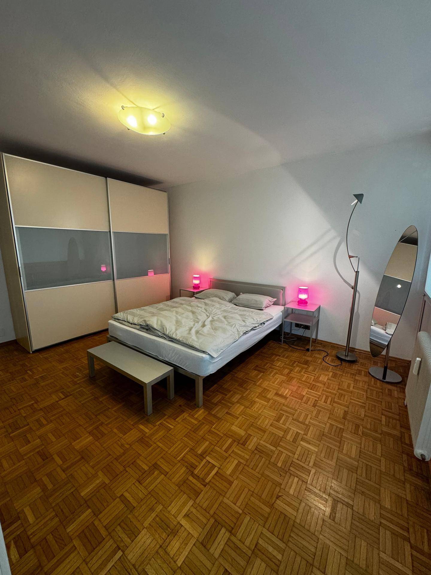 Schlafzimmer mit Parkettboden, Doppelbett, großem Kleiderschrank und dekorativer Beleuchtung.