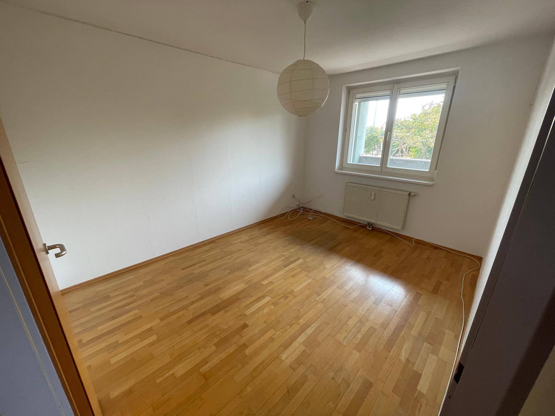Geräumiges Schlafzimmer mit Holzfußboden und Fenster, sorgt für viel Tageslicht und eine angenehme Wohnqualität.