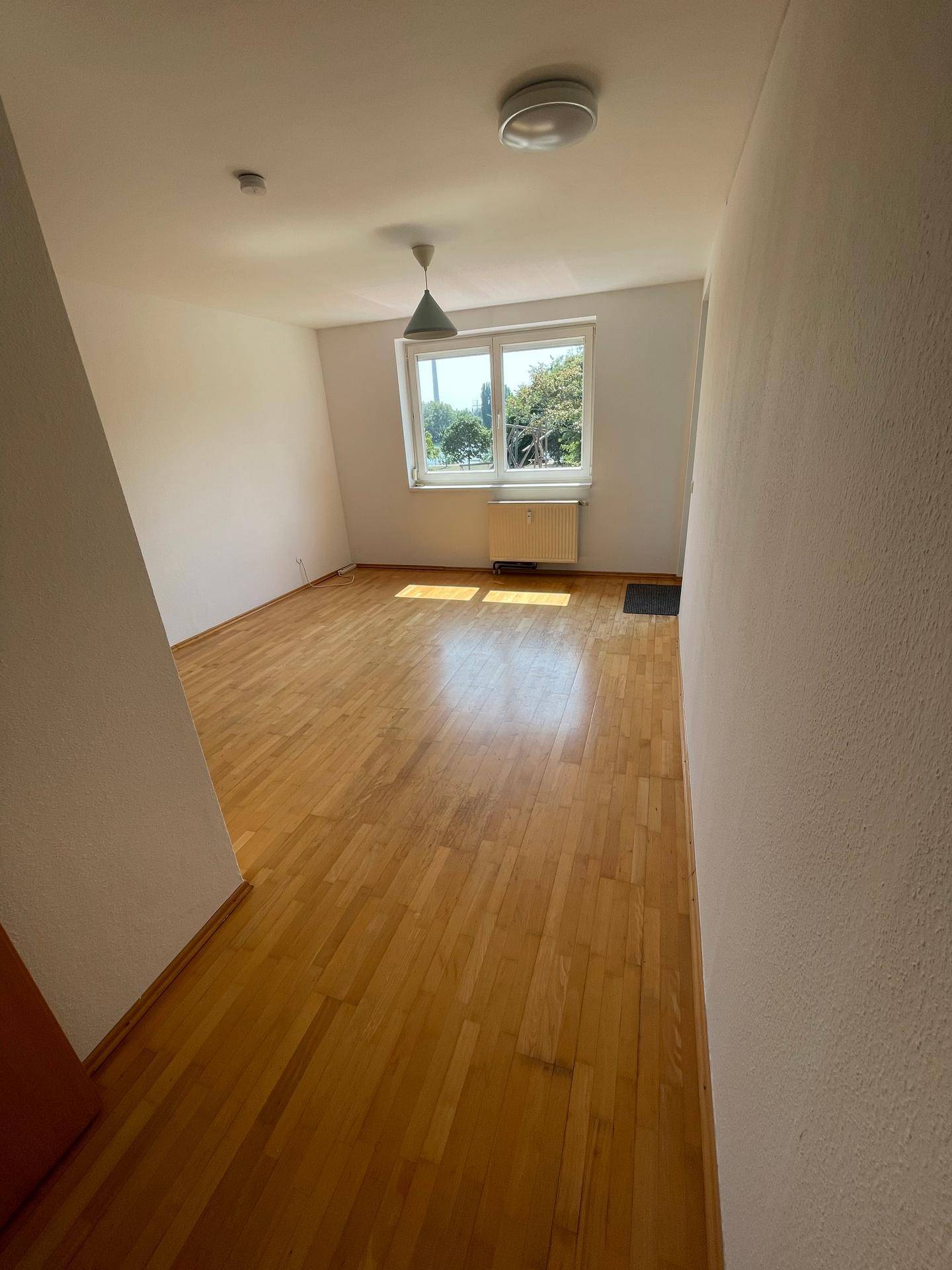 Geräumiges, helles Zimmer mit Holzfußboden und Blick ins Grüne, ideal als Wohn- oder Schlafzimmer.
