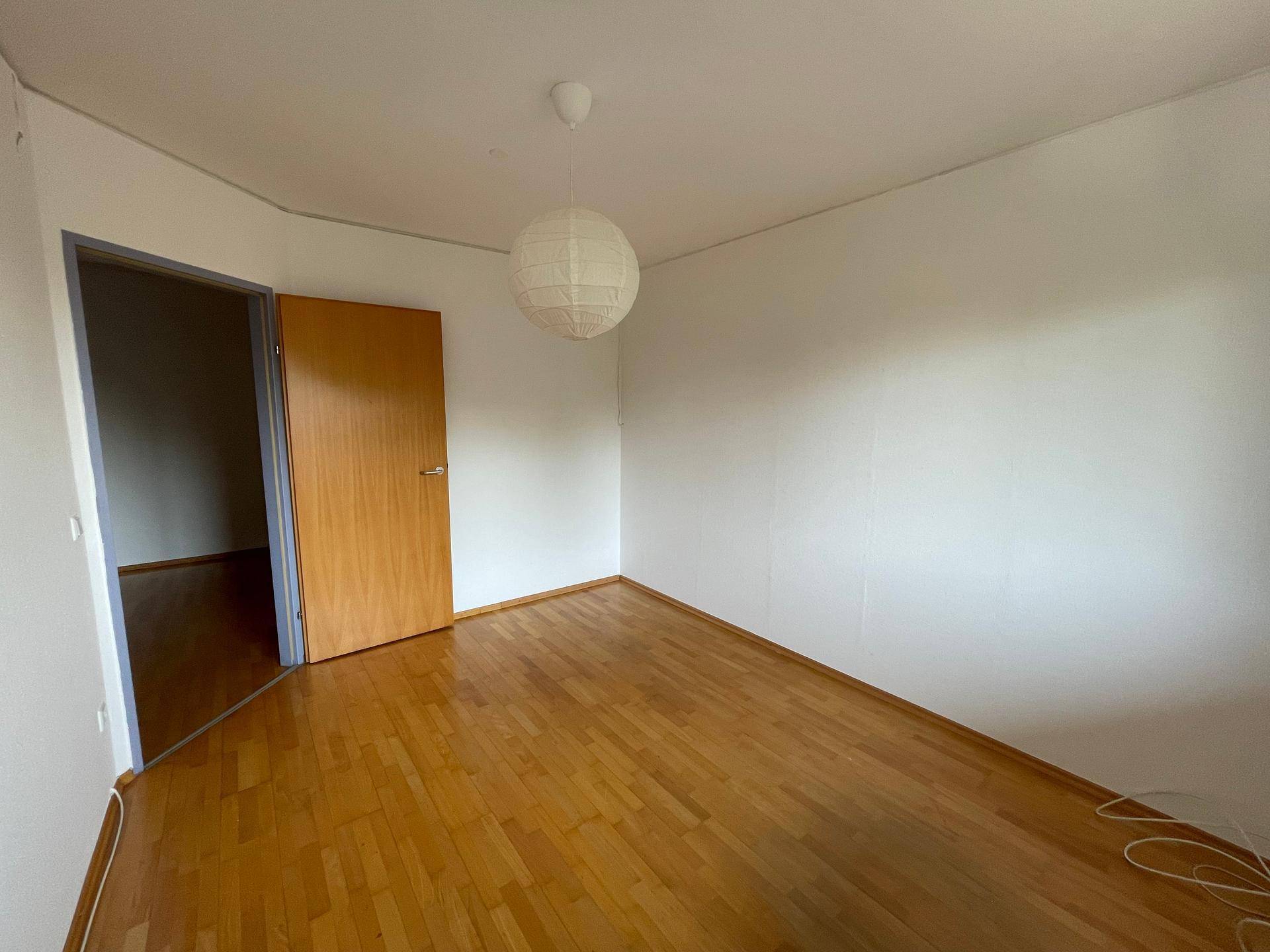 Leeres Zimmer mit Holzfußboden und einer Papierlampe, bereit zur individuellen Gestaltung.