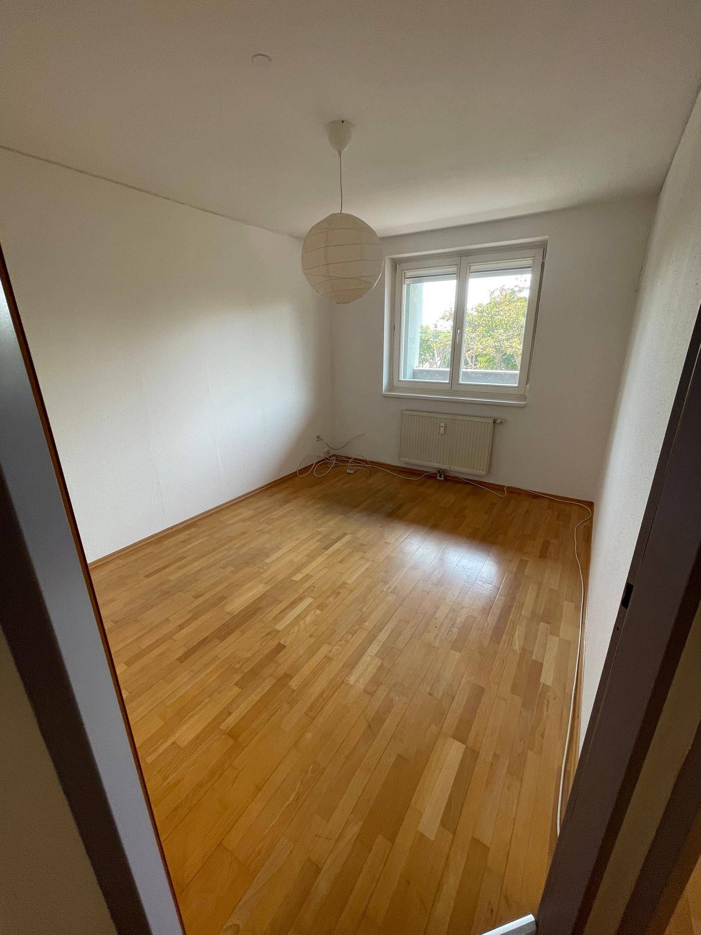 Helles Schlafzimmer mit Holzfußboden, großem Fenster und einer Papierlampe, bietet eine ruhige Atmosphäre.