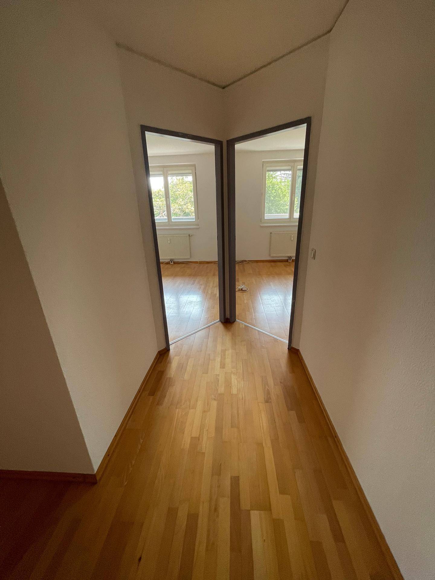 Flur mit Holzfußboden, der zu zwei identischen Zimmern mit Fenstern führt, bietet symmetrische Zugänge.