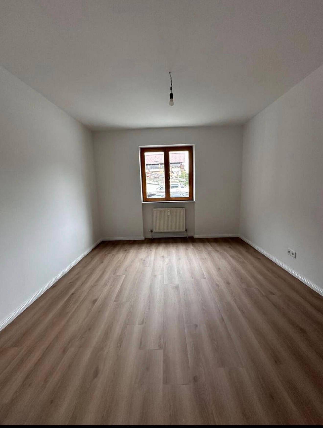 Heller, leerer Raum mit Laminatboden und einem Fenster, bereit zur individuellen Gestaltung.