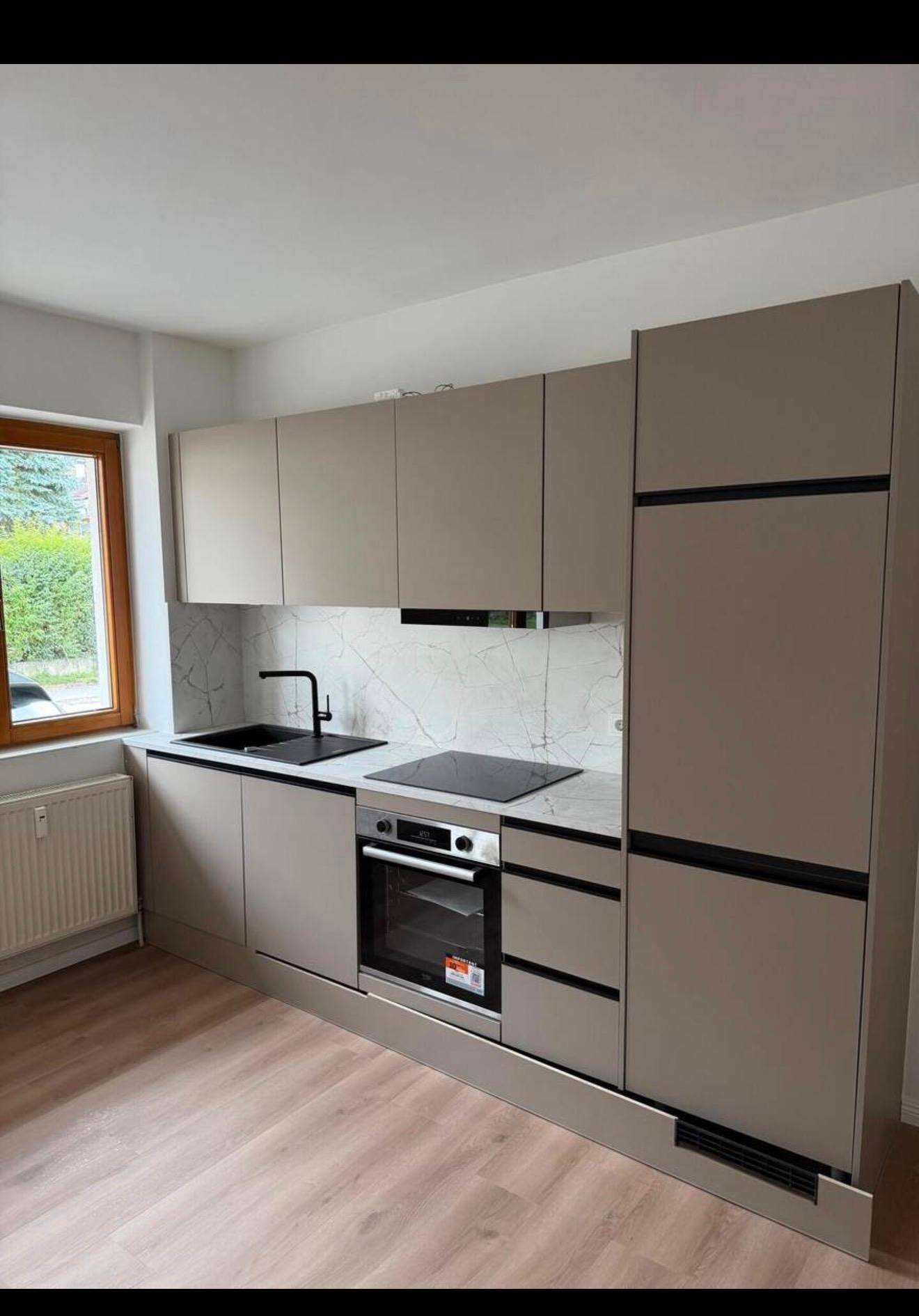 Kompakte, moderne Einbauküche mit hellen Fronten, Induktionskochfeld und integriertem Kühlschrank.