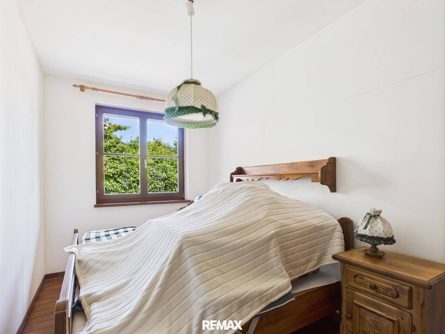 Gemütliches Schlafzimmer mit einem Einzelbett, Nachttisch und einem Fenster mit grüner Aussicht.