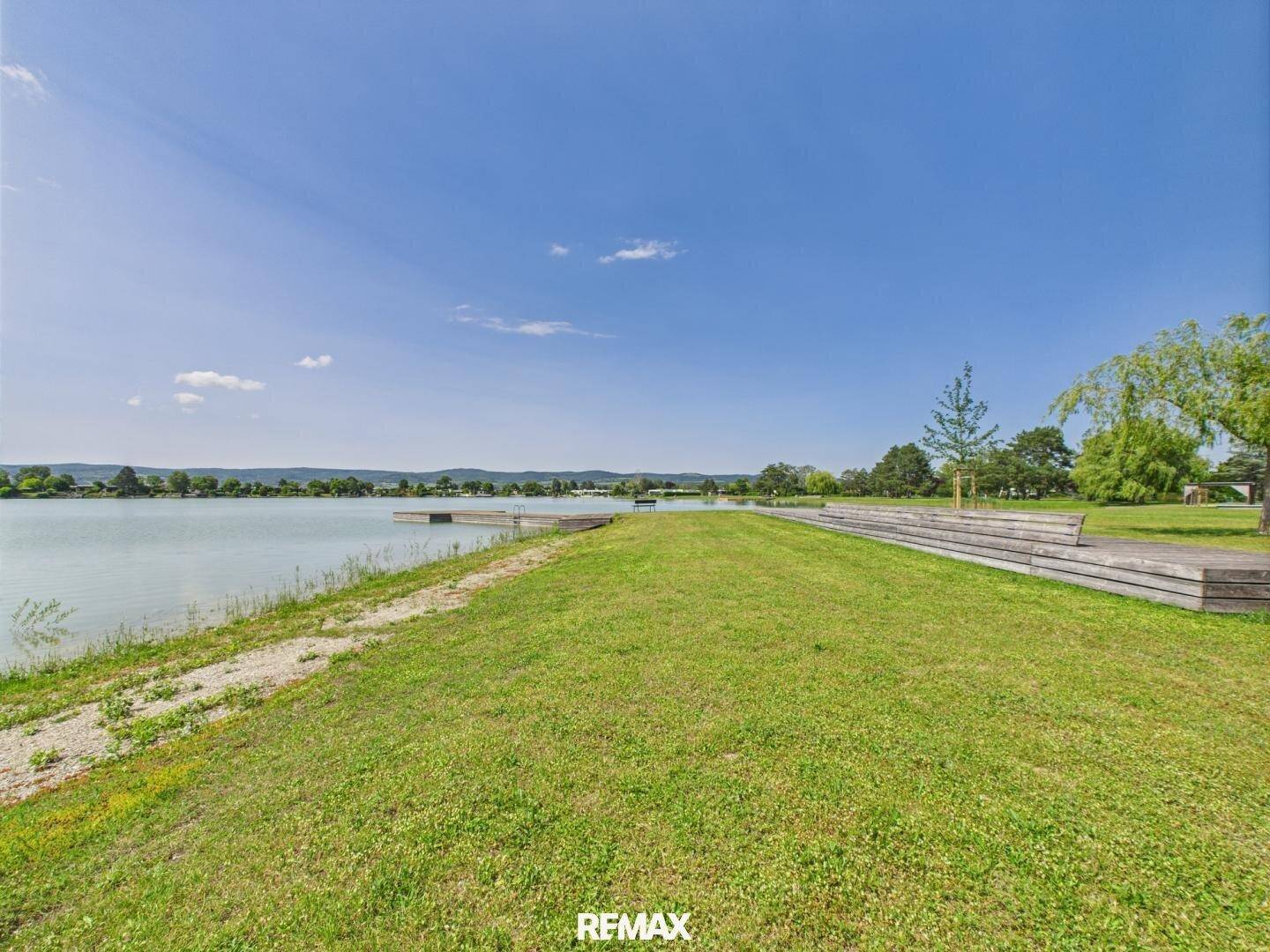 Malerischer Blick auf den See mit grünen Ufern und Holzstegen unter strahlend blauem Himmel.