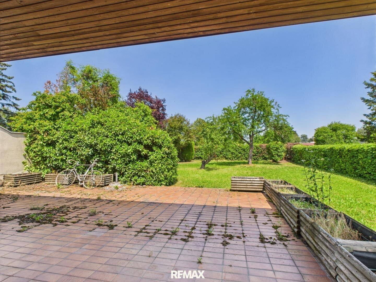 Große geflieste Terrasse mit Blick auf den Garten und viel Grün, ideal zum Entspannen.