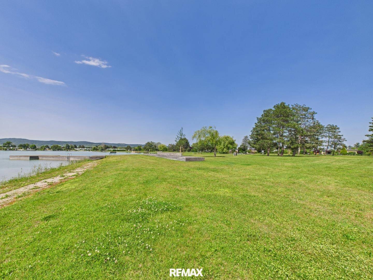 Panoramablick auf den See mit grünen Ufern und einem klaren blauen Himmel.