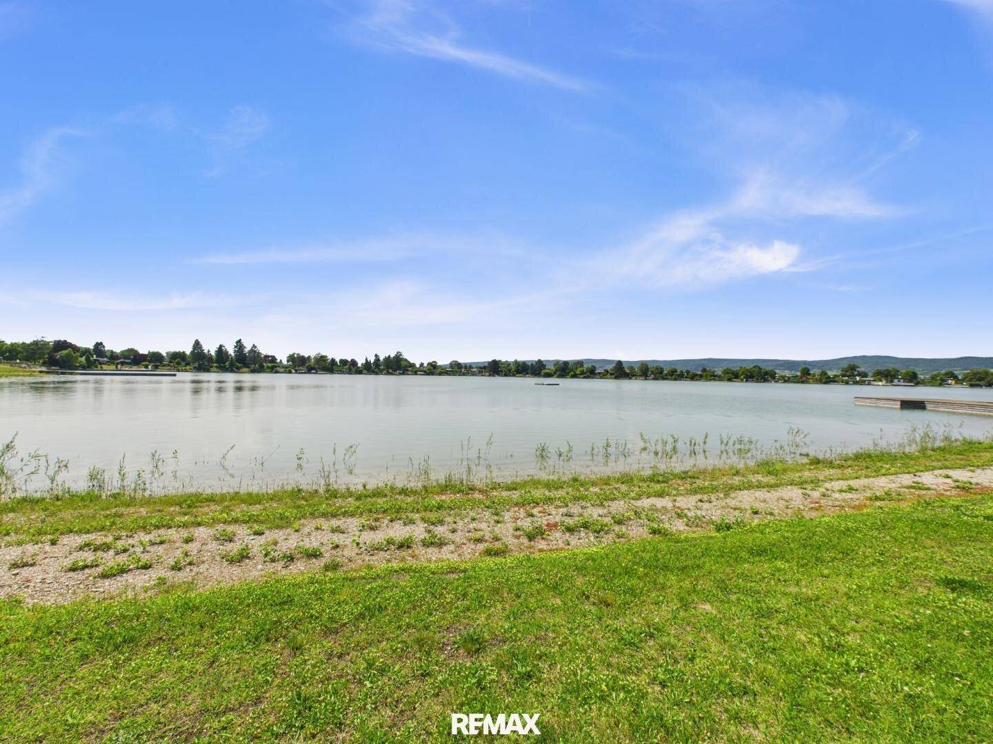 Breiter Blick auf die ruhige Seeoberfläche mit dem gegenüberliegenden Ufer in der Ferne.